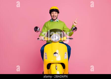 Porträt seines schönen, selbstbewussten fröhlichen fröhlichen Kerls, der mit dem Motorrad fährt, und Anzeige zeigt neue, über Rosa isolierte Neuheitslösung Stockfoto