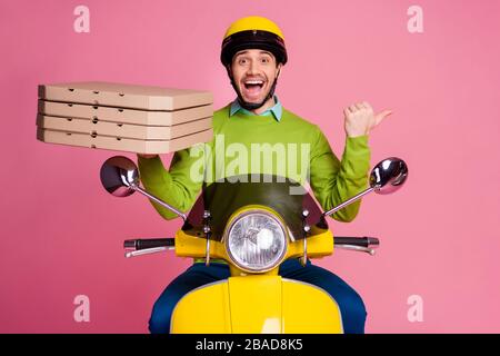 Porträt seines netten, lustigen fröhlichen fröhlichen fröhlichen, verblüfften Kerls, der mit Moped fuhr und Pizza brachte, die coole Werbung wertete und neue Lösung isoliert über Rosa zeigte Stockfoto