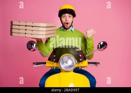 Porträt seines hübschen, lustigen und verblüfften Kerls, der mit Moped fährt und Pizza beiseite trägt, Werbung für neue Neuheit, isoliert über rosa Pastellfarben Stockfoto