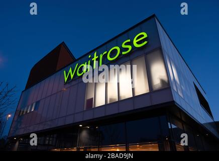 Das Waitrose Supermarkt Gebäude in Haywards Heath, West Sussex, England, nach Sonnenuntergang mit beleuchteten Schildern vor einem tiefen blauen Himmel. Stockfoto