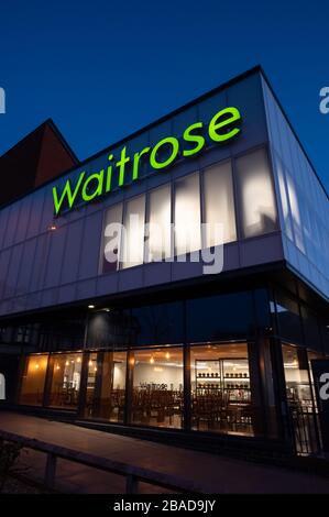 Das Waitrose Supermarkt Gebäude in Haywards Heath, West Sussex, England, nach Sonnenuntergang mit beleuchteten Schildern vor einem tiefen blauen Himmel. Stockfoto