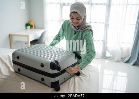 Schöne muslimische Frauen versuchten vor einer Urlaubsreise, ihren Koffer voller Kleidung auf dem Bett zu schließen Stockfoto