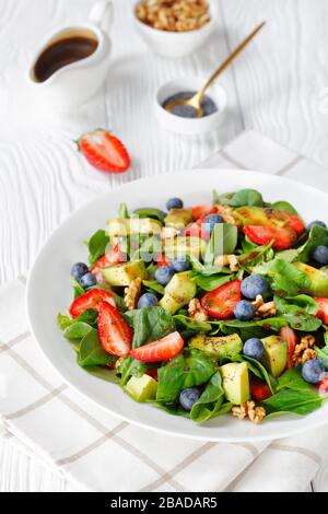Nahaufnahme von frischem Spinat Avocado-Walnüssen Erdbeere und Blaubeersalat mit Balsamico-Essig-Olivenöl und Mohnsamen, die auf einem weißen Teller anstehen Stockfoto