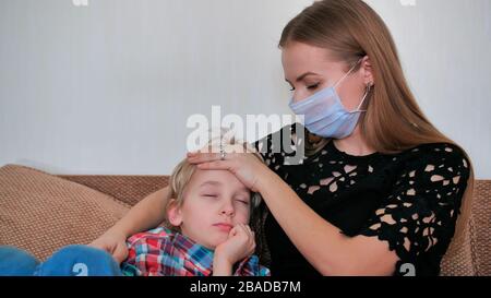 Eine fürsorgliche Mutter in einem Verband misst die Temperatur ihres Sohnes. Stockfoto