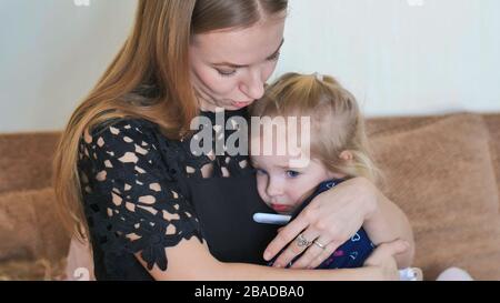 Die pflegende Mutter in einem Verband misst die Temperatur ihrer Tochter. Stockfoto