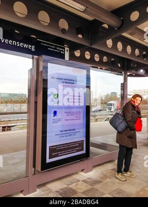 Amsterdam, Niederlande 17. märz 2020: Weibliche Reisende stehen vor einem öffentlichen Ansagebrett mit Regierungsempfehle zum Corona-Virus auf der Metrostation Amsterlveenseweg Plattform Stockfoto