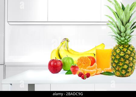 Gesundes Esskonzept - Gruppe verschiedener Früchte mit Glas Saft auf weißem Holztisch in einer modernen Küche Stockfoto