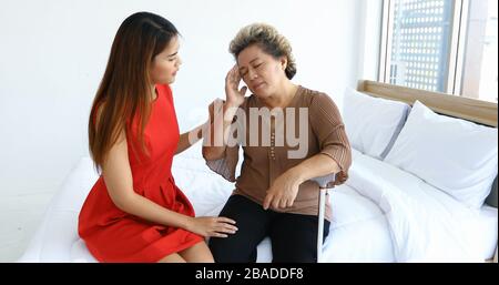 Fröhliche asiatin, die sich zuhause um ihre Großmutter im Schlafzimmer kümmert Stockfoto