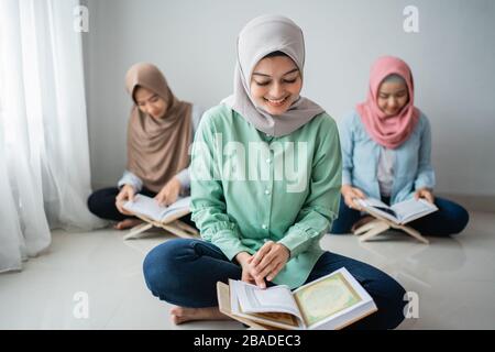Drei junge Frauen, die Hijabs tragen, lesen gemeinsam im Raum das heilige Buch des Korans Stockfoto