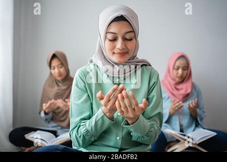 Drei asiatische Frauen sitzen und beten, um Gott zu danken, während sie lernen, den Heiligen Qur'an gemeinsam im Haus zu rezitieren Stockfoto