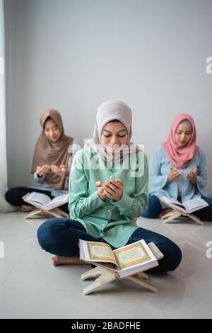 Drei verschleierte Frauen sitzen auf dem Boden und beten, während sie lernen, das heilige Buch des Al-Qoran gemeinsam im Haus zu lesen Stockfoto