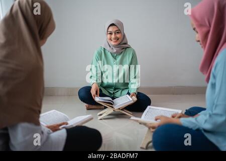 Drei verschleierte Frauen sitzen auf dem Boden, während sie gemeinsam im Haus den Qoran studieren Stockfoto