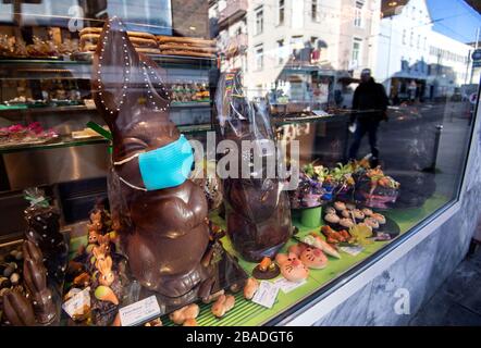 27. März 2020, Baden-Württemberg, Stuttgart: In einem Schaufenster einer Konditorei steht ein Schokoladenösterbündchen mit Gesichtsmaske, das Häuser reflektiert. Foto: Marijan Murat / dpa Stockfoto