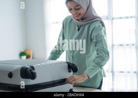 Schöne muslimische Frauen versuchten vor einer Urlaubsreise, ihren Koffer voller Kleidung auf dem Bett zu schließen Stockfoto