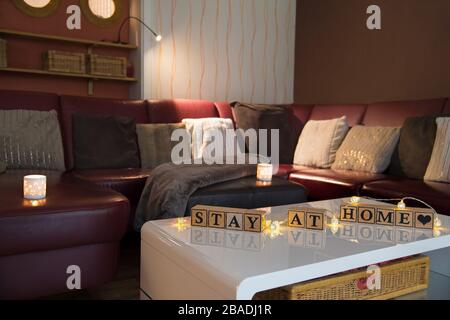 Infektionsrisiko mit Corona-Virus. Modernes Wohnzimmer, Tageslicht. Holzwürfel bilden den englischen Text bleiben zu Hause. Stockfoto
