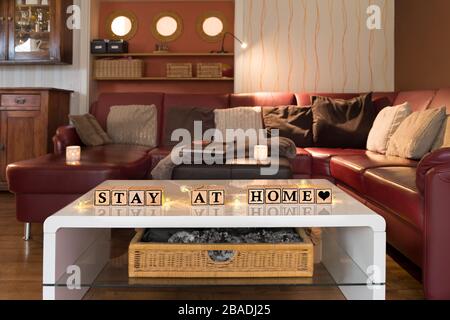 Infektionsrisiko mit Corona-Virus. Modernes Wohnzimmer, Tageslicht. Holzwürfel bilden den englischen Text bleiben zu Hause. Stockfoto