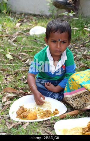 Ein kleiner Junge isst Mittagessen auf dem Boden im Dorf Kumrokhali, Westbengalen, Indien Stockfoto