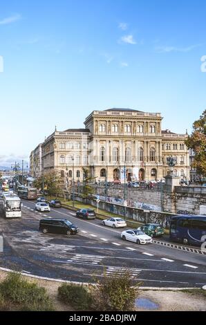 Budapest, Ungarn - 6. November 2019: Belebte Straße mit Autos in der Innenstadt der ungarischen Hauptstadt. Das Haus der ungarischen Akademie der Wissenschaften, MTA im Hintergrund. Vertikales Bild. Stockfoto