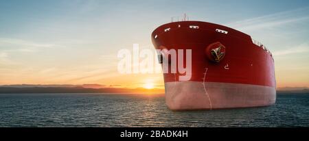 Nahaufnahme eines großen roten Handelsschiffs im Ozean. Bei Sonnenaufgang oder Sonnenuntergang. Ausführen von Export- und Importvorgängen für Frachtgüter. Ladung wird ausgeführt Stockfoto