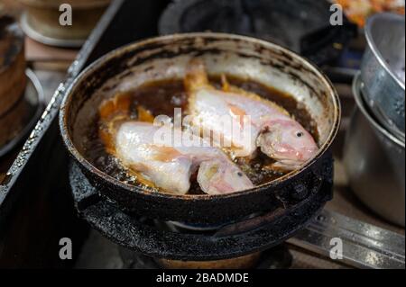 Zwei rote Tilapiefische, die in schmutziger Pfanne auf dem Herd braten Stockfoto