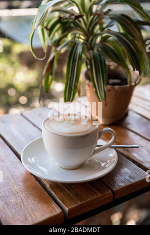 Heiße Latte mit Schaumblumenform und Pflanzendekoration an Holzbar im Café Stockfoto
