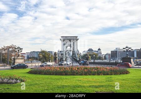 Budapest, Ungarn - Nov 6, 2019: Széchenyi Kettenbrücke in Budapest mit den angrenzenden Kreisverkehr, die zu den berühmten Wahrzeichen fotografiert. Autos, Verkehr. Gras und Blumen im Vordergrund. Stockfoto