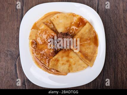 Pfannkuchen mit süßer Soße und Schokoladeneis auf einem weißen Teller. Platte mit Pfannkuchen auf einem Holztisch. Stockfoto
