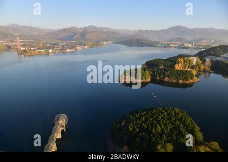 Vogelperspektive auf den Yanqi-See mit seinen ruhigen Gewässern, die große Pagode auf der anderen Seite des Sees und Teile der großen chinesischen Mauer kaum