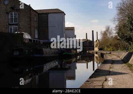 SALTAIRE, ENGLAND - 25/3/2020 - EIN Blick auf Mühlenkamine, die in der Entfernung von Saltaire von Shipley in einer traditionellen Kanalszene während der COVID-19 gesehen wurden Stockfoto