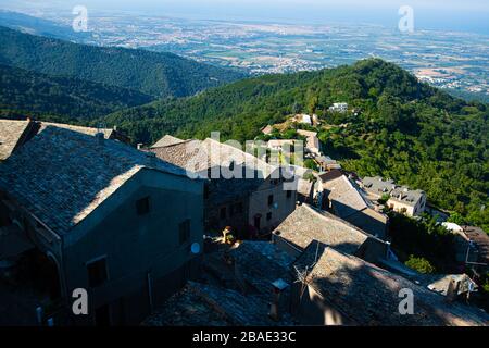 Hochwinkelblick auf ein korsisches Dorf in den Bergen mit Wald und Meer im Hintergrund Stockfoto