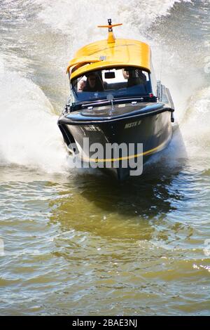 Nahaufnahme des schwarzen und gelben Wassertaxi, das in Richtung Kamera fährt und einen weckruf hinter sich lässt Stockfoto