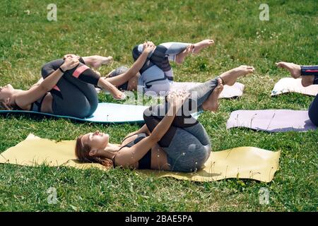 Gesunder Lebensstil. Frauen üben Yoga im Freien liegend auf Matte halten geknallte Beine geschlossen Augen lächelnd friedlich Stockfoto