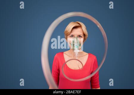 Coronavirus-Konzept. Blonde Frau in Oxigen Maske stehend isoliert auf blauen Spiraldraht suchen Kamera neugierig Stockfoto