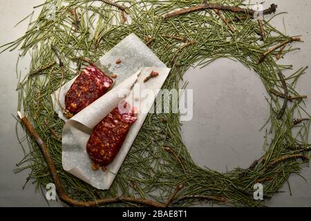 Getrocknete Wurst aus Biber-Fleisch auf Pergamentpapier und ein leerer Rahmen aus Nadeln. Zusammensetzung in einem Rahmen von Zweigen. Stockfoto