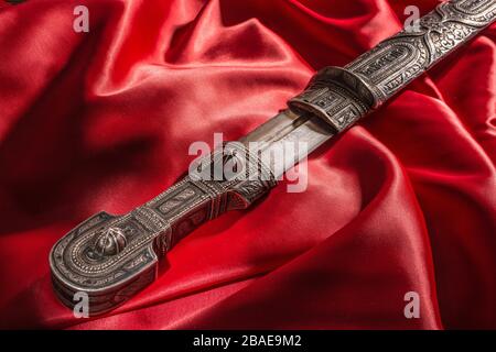 Wunderschönes Beispiel für kaukasischen Dolch mit Klinge in Form von Rom-Schwert auf rotem Seidenhintergrund. Jahrhundert (Zeit der russisch-kaukasischen Kriege (1816-1864 Stockfoto