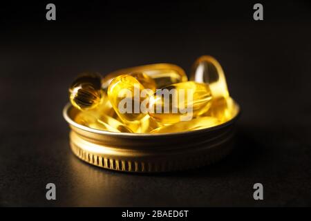 Makrofoto mit Omega-3-Kapseln in goldener Kappe auf schwarzem Hintergrund. Foto mit niedriger Taste. Medizin-, Gesundheits- und Apothekenkonzept. Stockfoto