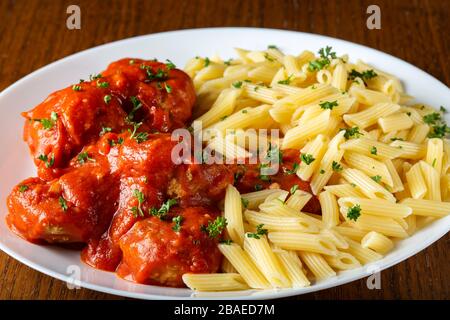 Fleischbällchen in Tomatensauce mit kleinen Penne Pasta auf dem Teller Stockfoto