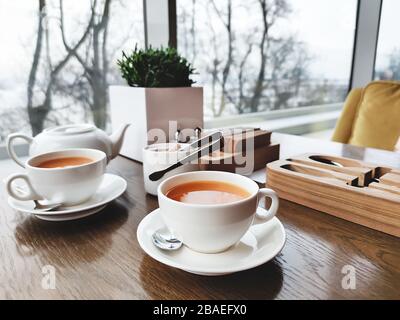 Zwei Tassen gesunder Kräutertee mit Meeresbuckthorn, Ingwer und Honig auf einem strukturierten, hellen Holztisch in einem Café mit modernem trendigen Interieur. Mockup für Stockfoto