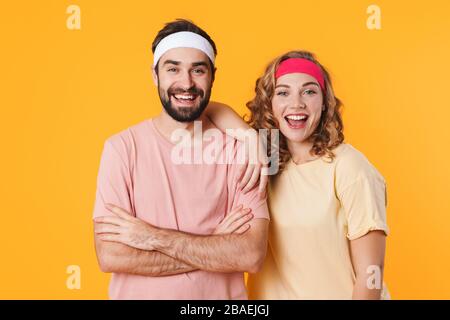 Porträt eines jungen, athletischen Paares, das Stirnbänder trägt, lächelnd und auf die Kamera blickt, die über gelbem Hintergrund isoliert ist Stockfoto