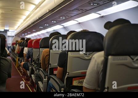 Blick auf eine Seite des Fluggangs eines Flugzeugs von der Rückseite der Sitze. Blaue und rote Kopfstützen Stockfoto