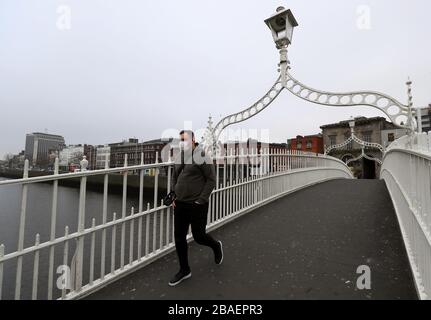 Ein Mann, der eine Gesichtsmaske trägt, spaziert über eine fast menschenleere ha'Penny Bridge im Stadtzentrum Dublins, da Irland eine Reihe von weitreichenden Maßnahmen eingeführt hat, um die Ausbreitung des Coronavirus einzudämmen. Stockfoto