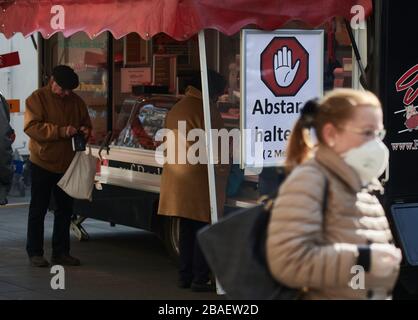 München, Deutschland. März 2020. "Halten Sie Ihre Distanz!, 2 Meter", fügte ein Markthändler ein Schild an seinem Wurststand an. Zur Eindämmung des Coronavirus hat NRW alle Ansammlungen von drei oder mehr Menschen in der Öffentlichkeit verboten. Credit: Bernd Thissen / dpa / Alamy Live News Stockfoto