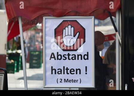 München, Deutschland. März 2020. "Halten Sie Abstand! 2 Meter hat ein Markthändler an seinem Wurststand mit einem Schild befestigt. Zur Eindämmung des Coronavirus hat NRW alle Ansammlungen von drei oder mehr Menschen in der Öffentlichkeit verboten. Credit: Bernd Thissen / dpa / Alamy Live News Stockfoto