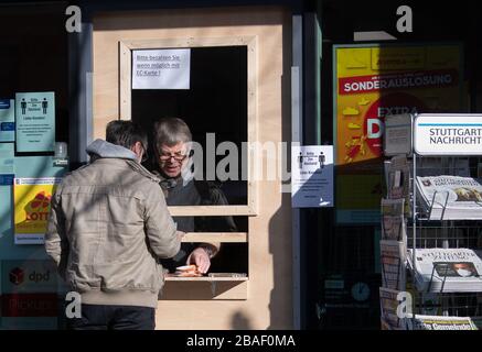 27. März 2020, Baden-Württemberg, Stuttgart: Volker Suchanek, Inhaber des Einzelhandelshauses Abele Tabakwaren, betreut einen Kunden hinter einem Schutz von Holz und Plexiglas. Die Nachfrage in Deutschland nach Zeitungen und Zeitschriften verschiebt sich derzeit aufgrund der Coronavirus-Krise. Foto: Marijan Murat / dpa Stockfoto