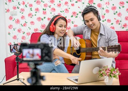 Asiatischer Vlogger von Ehepaaren, der die Musik über das Handy über den Kanal der sozialen Medien an die Teilnehmer weitergibt und diese weitergibt, Kommentar über Laptop, Kamera überprüfen Stockfoto