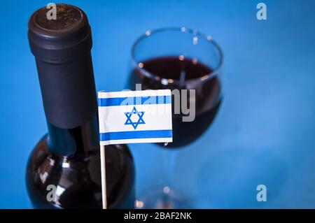 Ein Glas Rotwein mit einem Stück blauen Käse auf einem kleinen Teller mit einer winzigen Flagge Israels auf blauem Hintergrund. Israelisches Weinkonzept, hergestellt in Israel Stockfoto