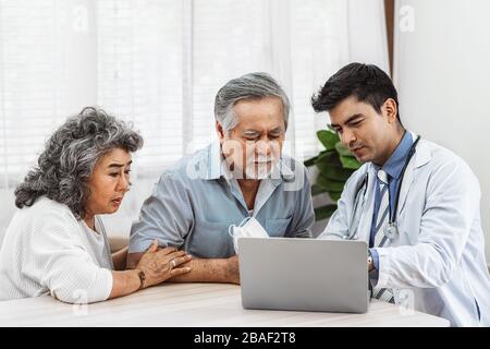 Doktor, der mit einem technischen Laptop spricht, um den asiatischen Großeltern-Patienten im Haus, die Gesundheitsversorgung mit der Gesellschaft für lange Leben und ältere Menschen auszukultivieren Stockfoto