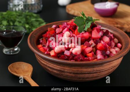 Traditionelle russische Salatvinaigrette mit Bohnen, Pickeln und gekochtem Gemüse in einer Tonschale vor dunklem Hintergrund, vegetarische Speisen Stockfoto