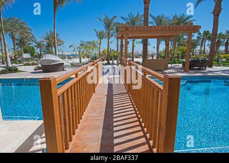 Sonnenliegen auf der luxuriösen, tropischen Hotelresort-Zimmerterrasse am Pool mit Holzbrücke Stockfoto