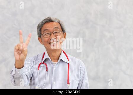 Portrait des chinesischen Arztes gesunder alter Mann asiatischer Ältester steht lächelnd Hand Siegeszeichen mit Platz für Text. Stockfoto